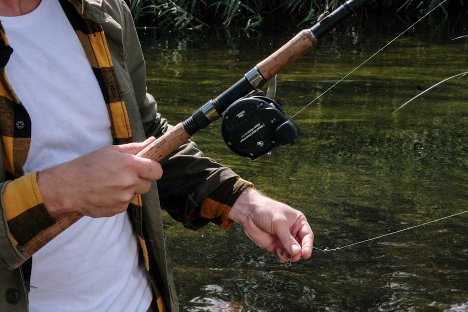 Close-up of a man fishing on a tranquil river, showcasing a fishing rod and reel.